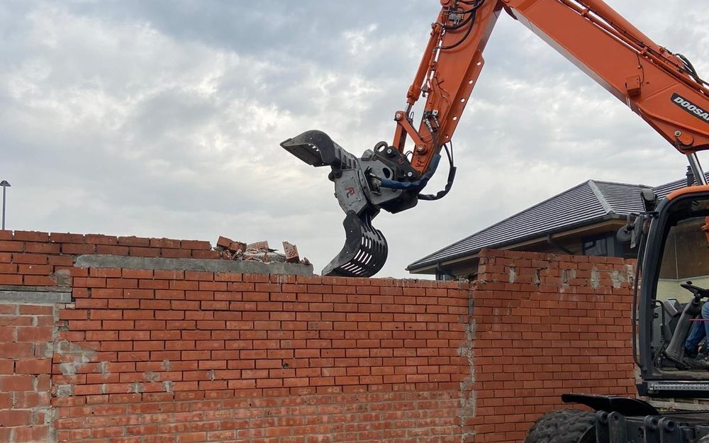 Afbraakwerken door AST BV — sloopkraan breekt een bakstenen muur af in de provincie Antwerpen